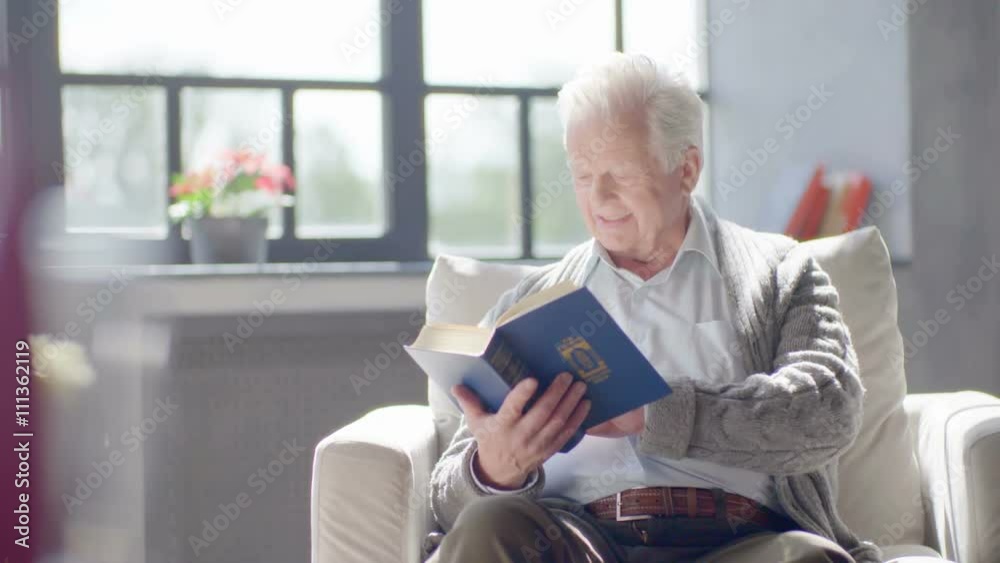 elderly caucasian man reading a book and drinking a delicious tea in a modern apartment elderly caucasian man reading a book and drinking a delicious tea in a modern apartment