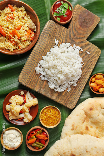 Boiled and fried rice with vegetables, flat bread on banana leaf background