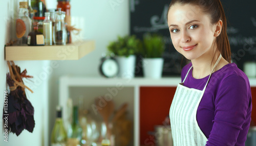 Young woman standing in her kitchen near desk with shopping bags