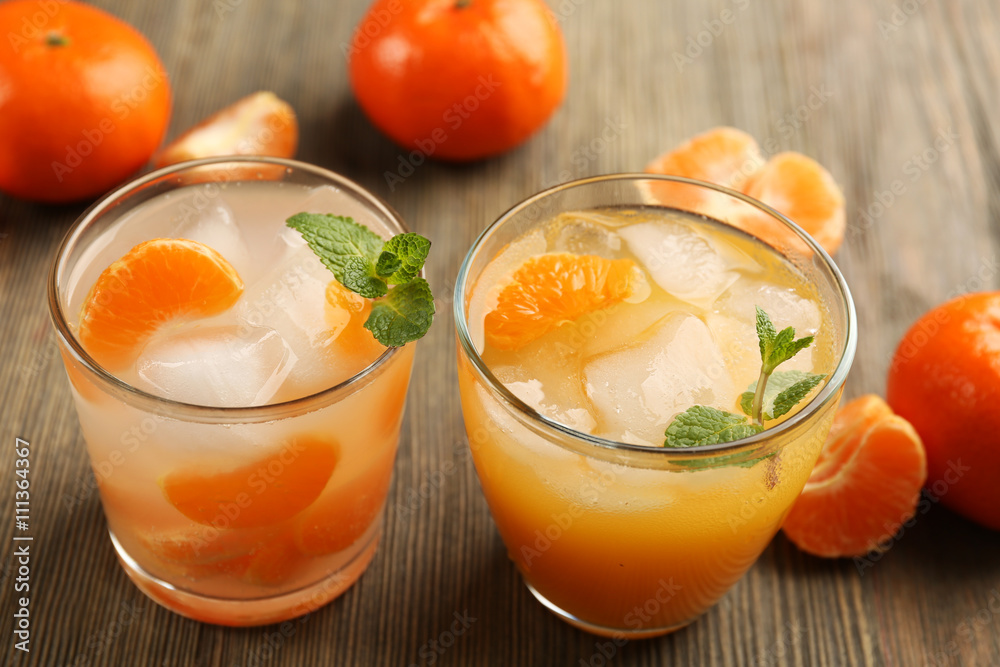 Two fresh delicious tangerine cocktails with ice, mint and mandarins on the wooden table, close up Two fresh delicious tangerine cocktails with ice, mint and mandarins on the wooden table, close up