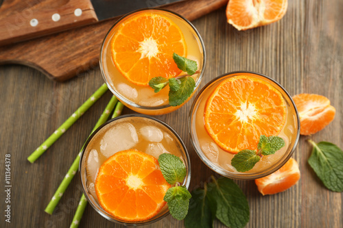 Delicious tangerine cocktails with sliced mandarins, ice, garnished with a mint, served on a wooden table, top view