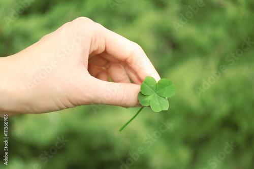 Female hand holding clover leaf on meadow background