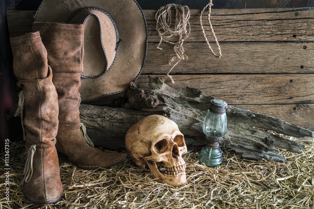 Still life with human skull on hay with traditional leather boots and  american west rodeo brown cowboy hat background, vintage and dark tone for  horror halloween Photos | Adobe Stock