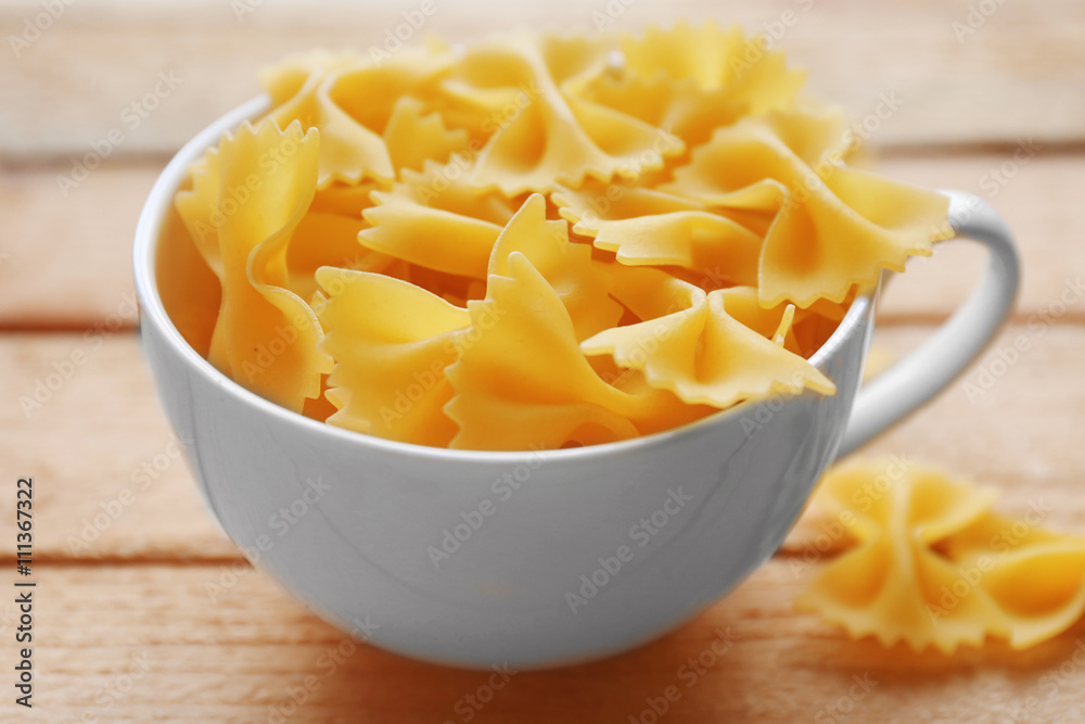 Pasta farfalle in cup on wooden table background Pasta farfalle in cup on wooden table background