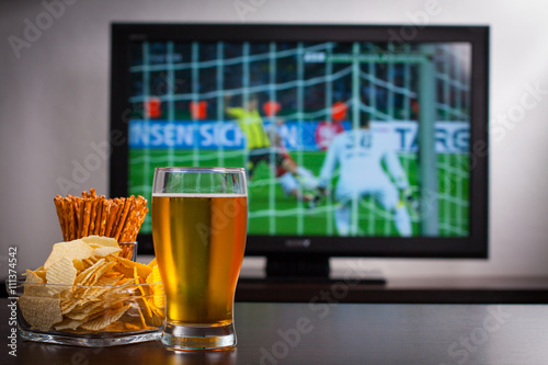 Pint of beer, chips and salty sticks on the tabele in front of televisor show off football..Set of snacks and beverage soccer fan at home. photo