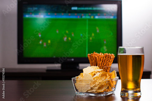 Pint of beer, chips and salty sticks on the tabele in front of televisor show off football..Set of snacks and beverage soccer fan at home. photo