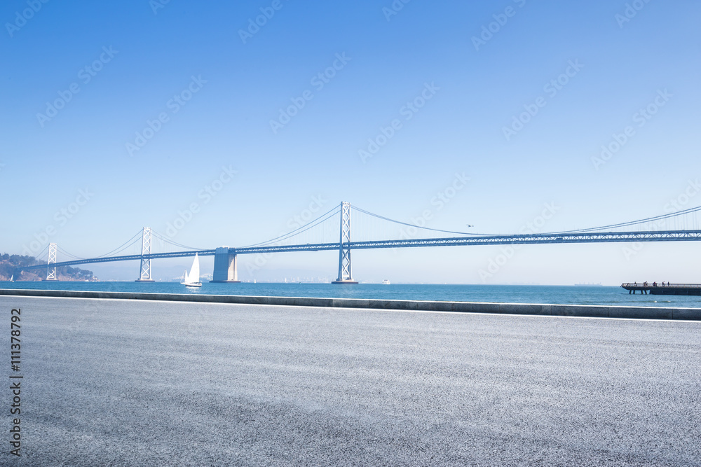 empty asphalt road near sea with gold gate bridge in blue sky