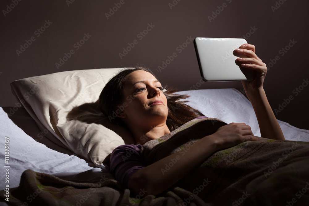 Young woman relaxing in her bed before sleep. She is using digital tablet. Young woman relaxing in her bed before sleep. She is using digital tablet.