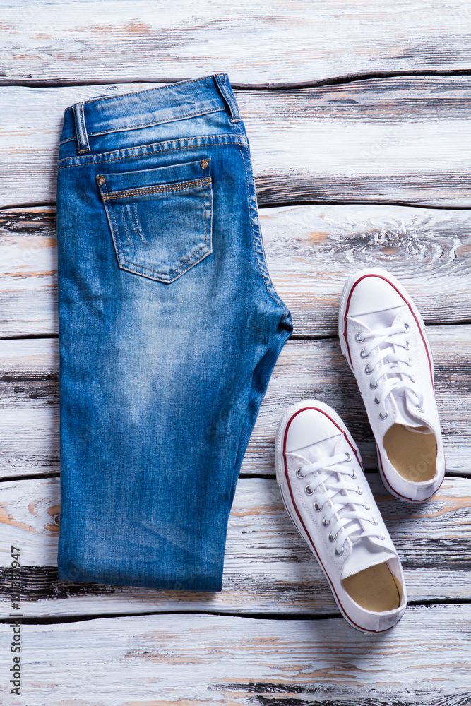 Folded jeans and white shoes. Blue denim pants with footwear. Quality  casual shoes on display. Canvas footwear for women. Stock Photo