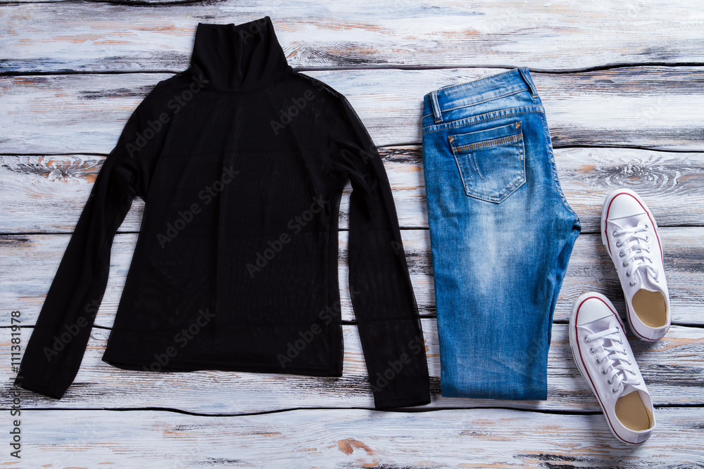 Black top with blue jeans. White canvas shoes and pants. Outfit with high  collar top. Female clothing on wooden table. Stock Photo | Adobe Stock