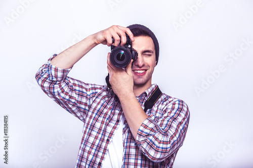 Say cheese! Young man focusing at you with digital camera while standing in studio on gray background
