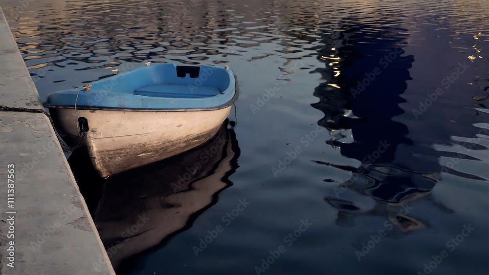 Boat at the quay moorage at sunset reflecting in water in the evening twilight dusk. Summer warm and calm concept.