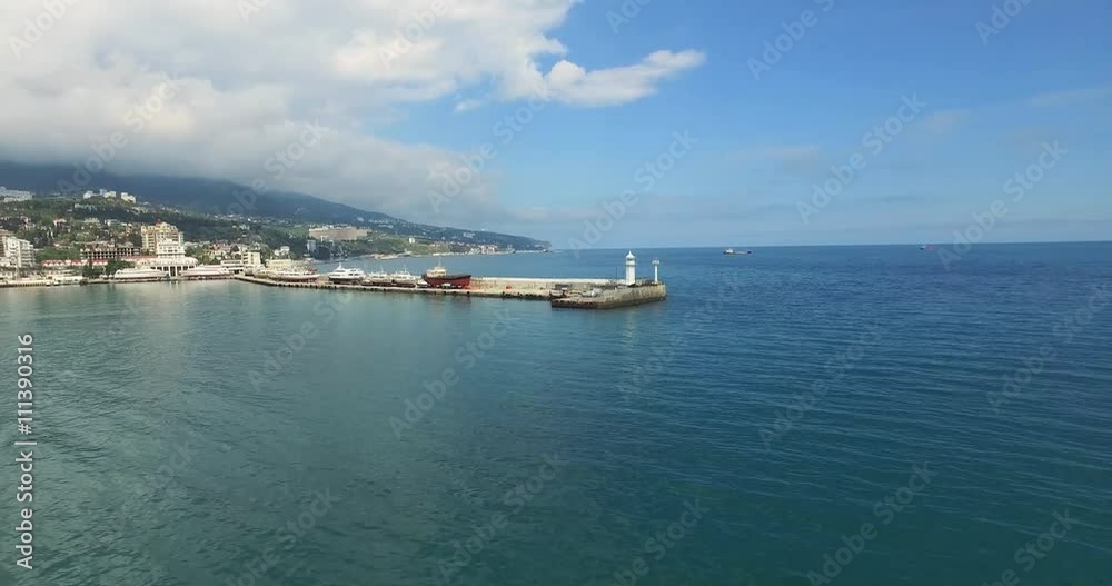Aerial view of the small white lighthouse on the pier at the harbour. Shoot is made on the peninsula of Crimea Aerial view of the small white lighthouse on the pier at the harbour. Shoot is made on the peninsula of Crimea