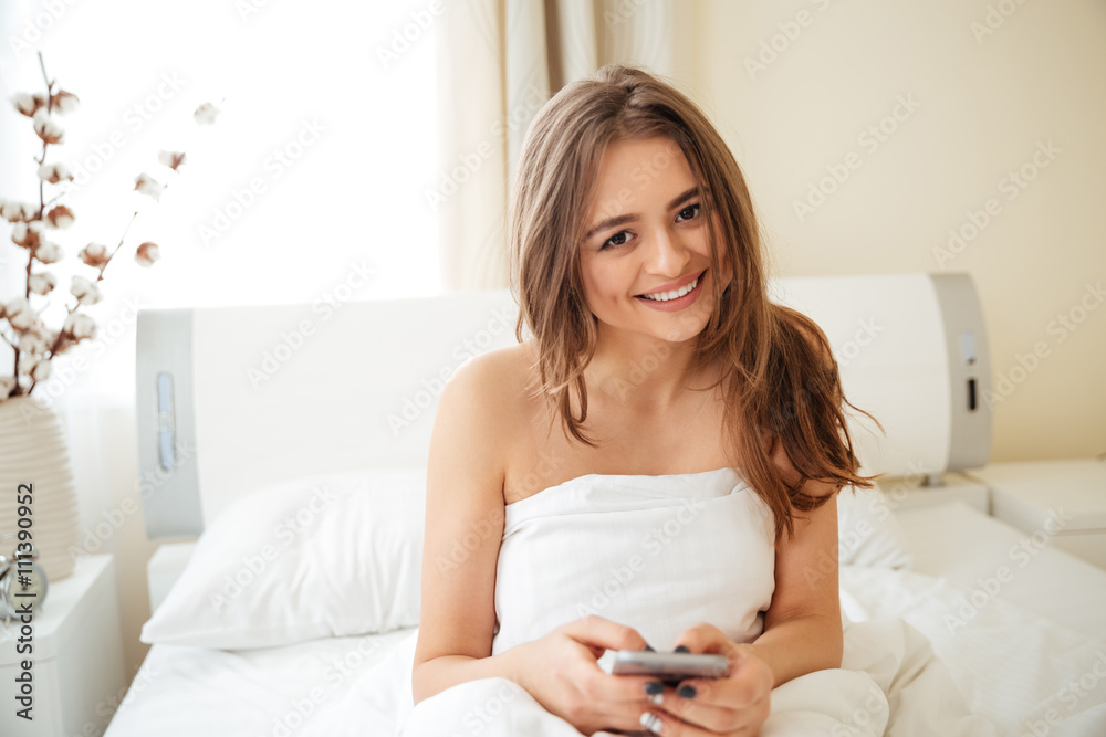 Woman sitting on the bed and using smartphone Woman sitting on the bed and using smartphone