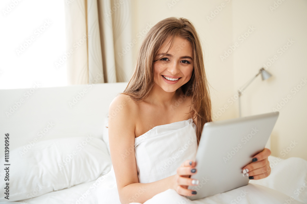 Woman sitting on the bed and using tablet computer Woman sitting on the bed and using tablet computer