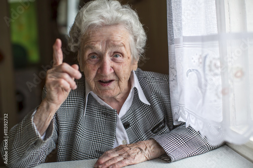 An elderly woman sitting at a table and specifies the finger.