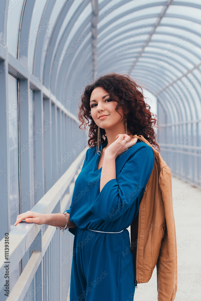 Beautiful curly-haired woman in a long dress on a light background