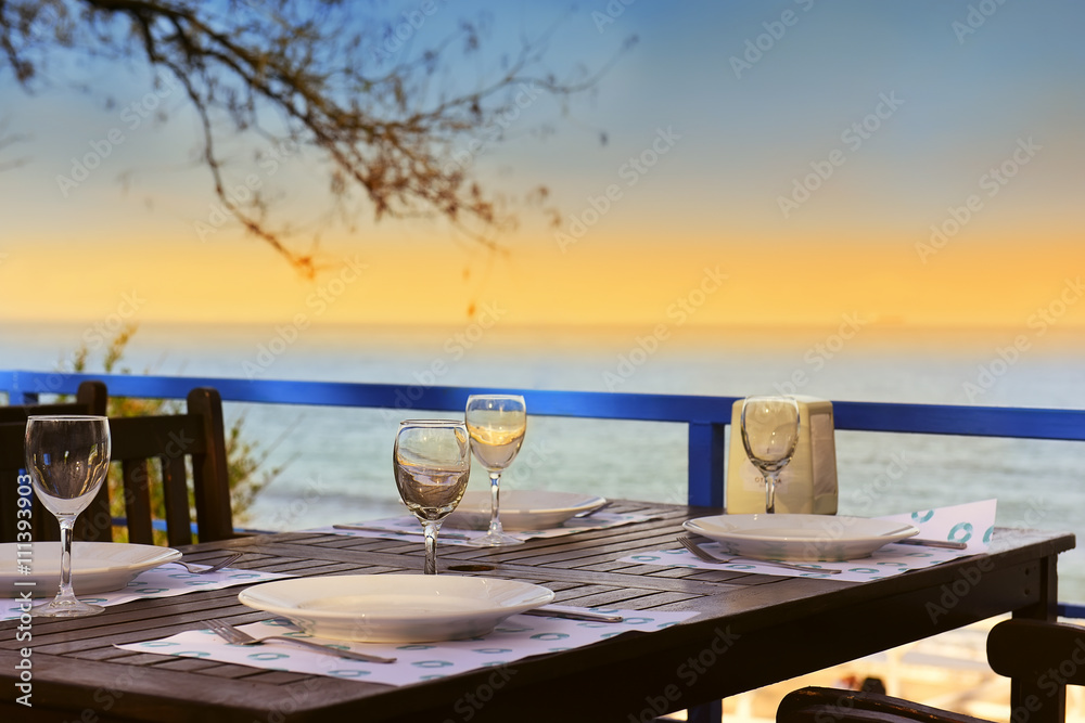 served table on the sea shore. glasses, plates, coasters saucer on brown wooden table. In the background, the sea and the light  sunset. pryaitny warm evening, the place to meet and talk