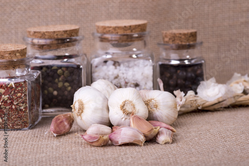 fresh garlic surrounded by containers with herbs