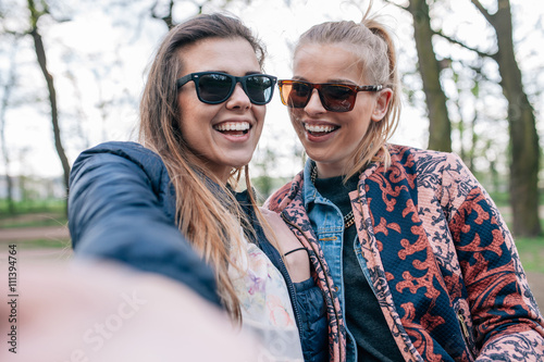 Two girl sitting on the bech in the park and taking selfie.