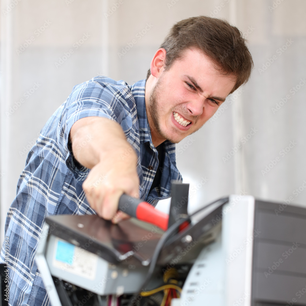Aggressive man hitting a computer with a hammer