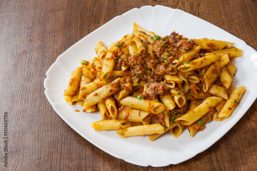 pasta penne with stew meat sauce in a plate on wooden table pasta penne with stew meat sauce in a plate on wooden table