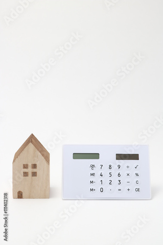Miniature house and calculator on white background.