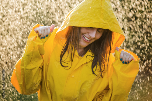 Bild auf Leinwand Portrait of happy woman wearing yellow raincoat enjoying the rain