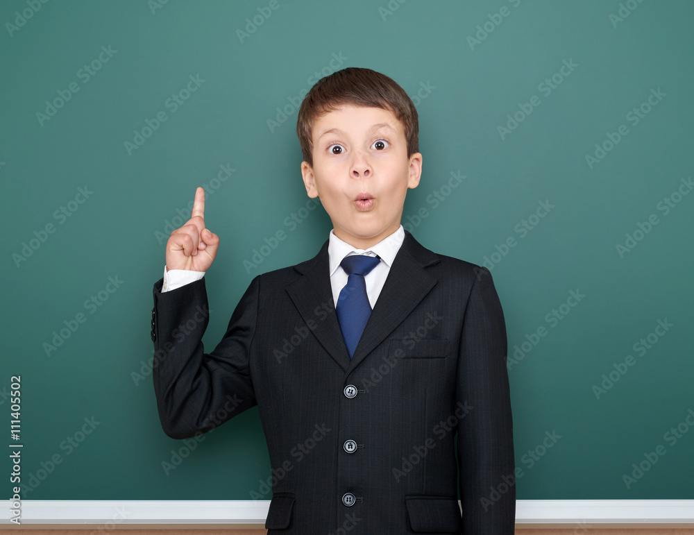 school boy in black suit show finger up gesture and wonder, point on green chalkboard background, education concept school boy in black suit show finger up gesture and wonder, point on green chalkboard background, education concept