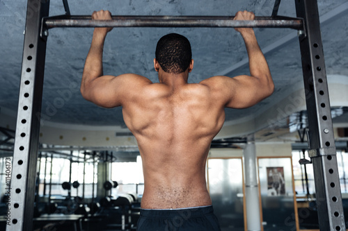 Shirtless fitness man doing stomach exercises on a horizontal bar