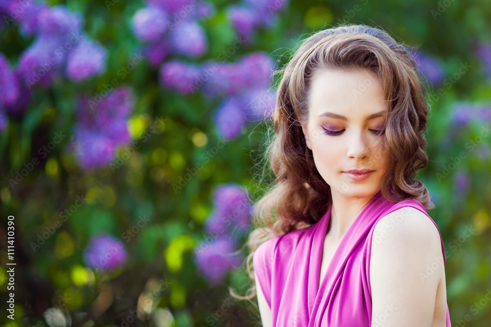 Fototapeta premium Young beautiful girl posing near lilac bushes in blossom