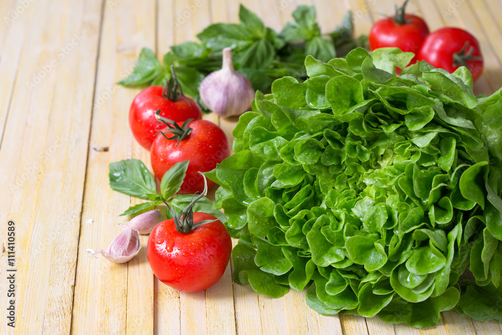 Fresh lettuce, tomato, basil and garlic for a light summer salad on a wooden surface, selective focus Fresh lettuce, tomato, basil and garlic for a light summer salad on a wooden surface, selective focus