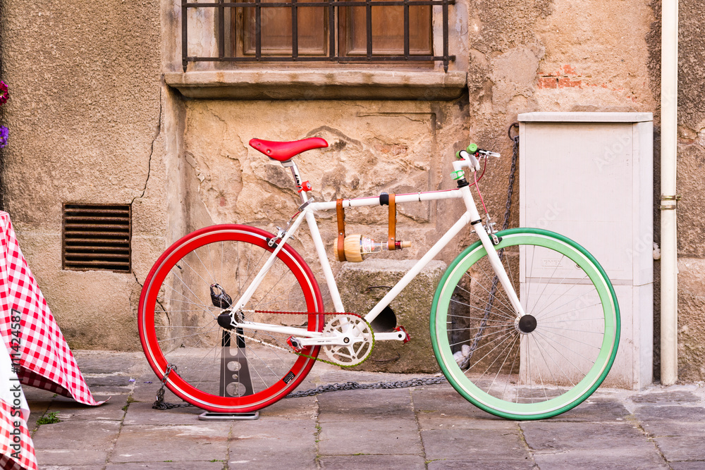 A bicycle with the colors of the Italian flag next to a wall in