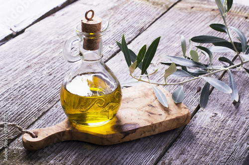 Jug with extra virgin olive oil on cutting board surrounded by branches