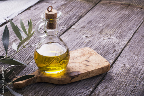Jug with extra virgin olive oil on cutting board surrounded by branches