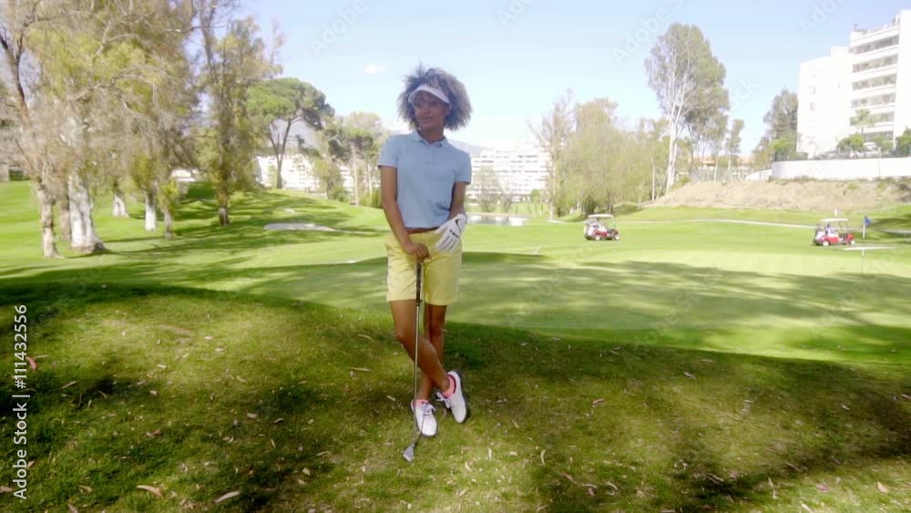 Attractive young woman golfer standing watching leaning on her club with crossed legs as she waits for her turn to play Attractive young woman golfer standing watching leaning on her club with crossed legs as she waits for her turn to play