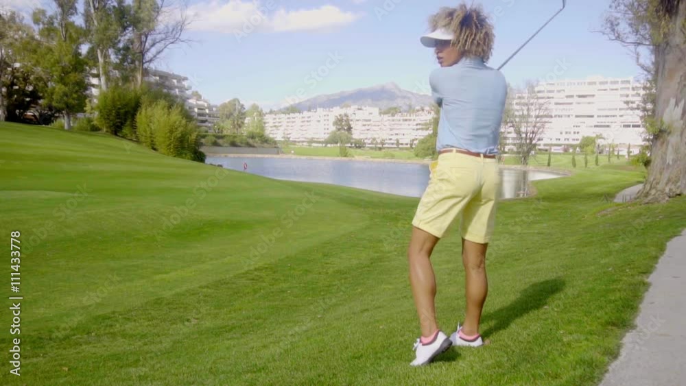 Young woman golfer lining up her golf shot on the fairway with a lake and urban development behind her Young woman golfer lining up her golf shot on the fairway with a lake and urban development behind her