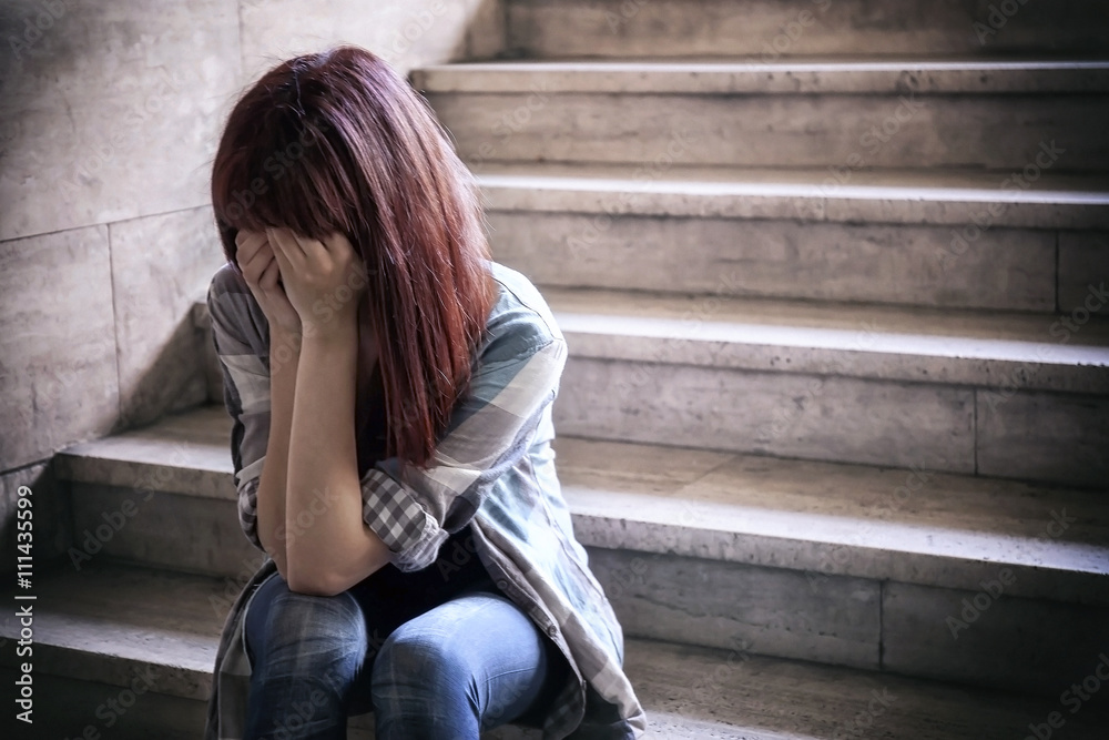 Depressed girl. Adolescent crisis sitting on the steps of a basement, covers her face with her hands.