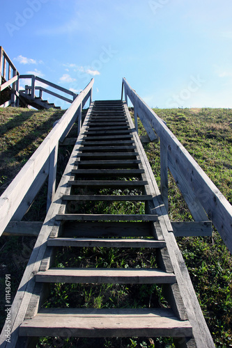 Fototapeta Naklejka Na Ścianę i Meble -  grey long wooden staircase with wooden railings on the green hil