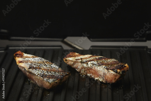 two pieces of salmon roasted close up on home electronic grill plate tasty diet fish meal