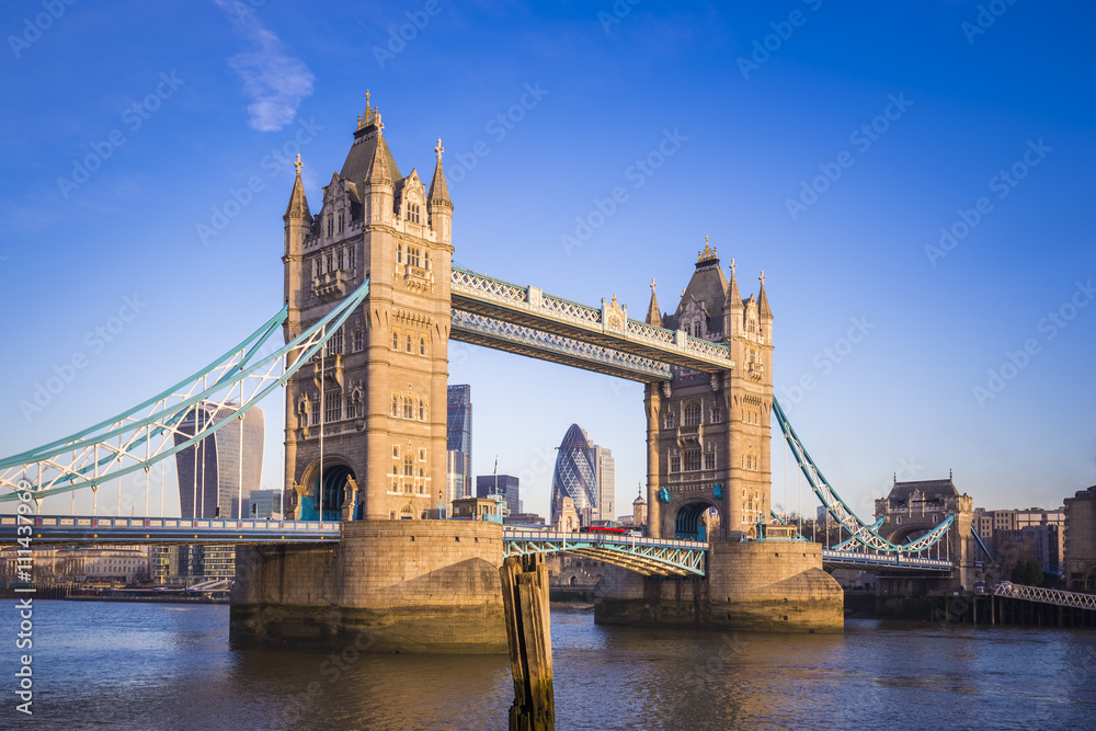 London, England - Iconic Tower Bridge in the morning sunlight with Red Double Decker bus and Bank District at background
