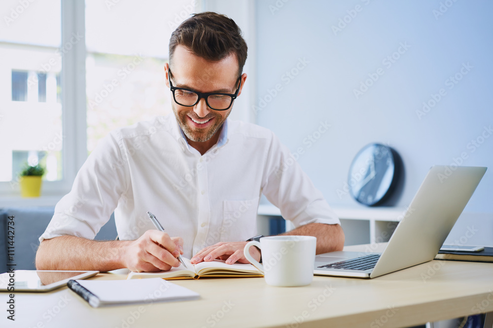 Happy man working from home office doing notes sitting at desk Happy man working from home office doing notes sitting at desk