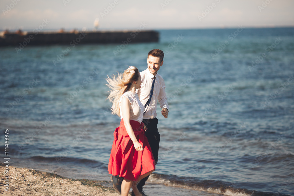 Young happy couple walking on beach smiling holding around each other. Love story Young happy couple walking on beach smiling holding around each other. Love story