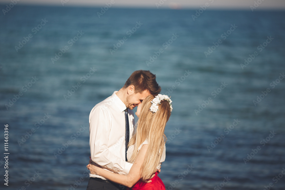 Young happy couple walking on beach smiling holding around each other. Love story