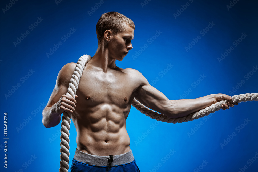 Obraz premium Fit young man with beautiful torso and a rope on blue background