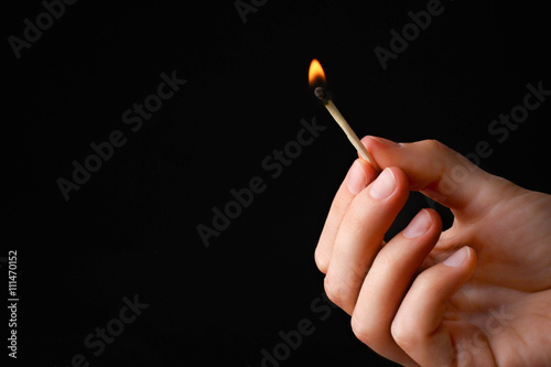 girl holding burning match in hand on black wooden background photo