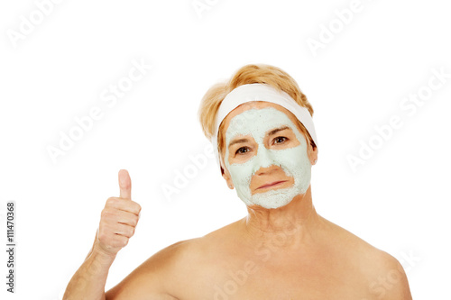 Smile elderly woman with facial mask shows thumb up