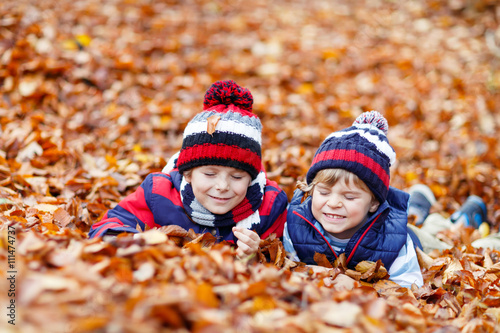 Two little kid boys lying in autumn leaves, in park.