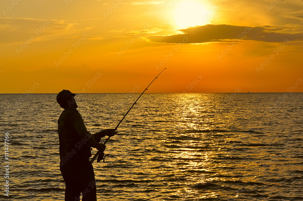 silhouette of fisherman in sunset, dawn light casting a fishing rod from the sea shore. orange-red paint dawn. sun over the water.
