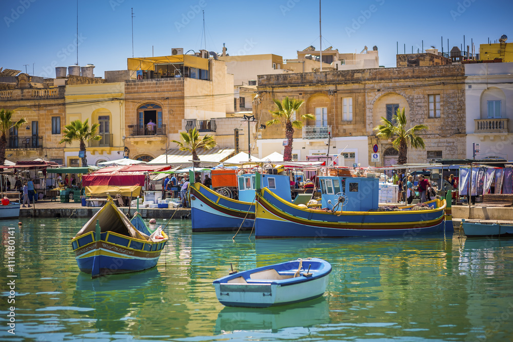 Malta - Traditional colorful Luzzu fishing boats at Marsaxlokk on a sunny summer day with blue sky and green sea